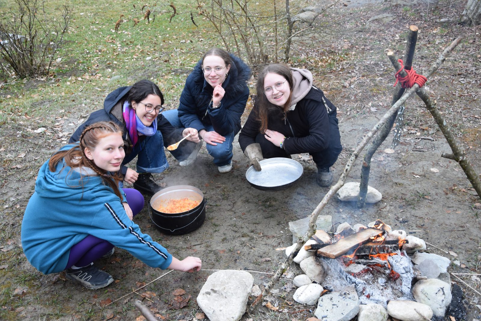Vier Kursteilnehmerinnen kochen ihr Essen über dem Lagerfeuer.