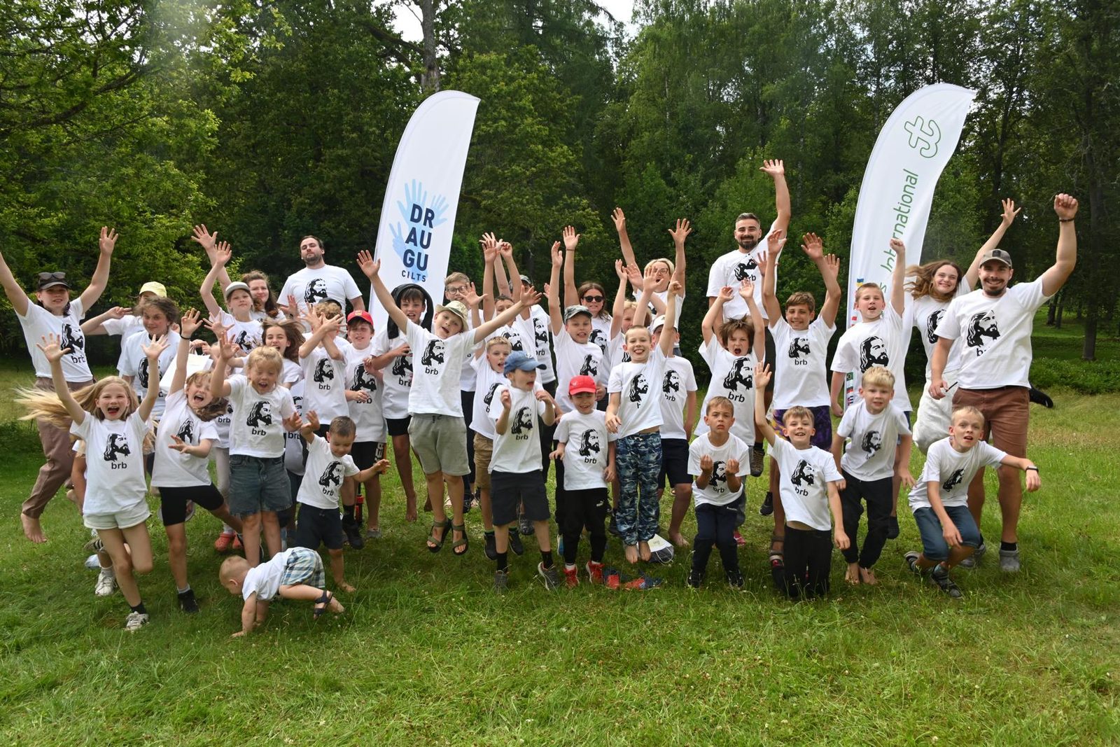 Die Lagergruppe jubelt vor den Fahnen der lettischen Jungschar und von Youngstars International.